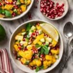 Two bowls of cucumber mango salad with a small bowl of pomegranate seeds.