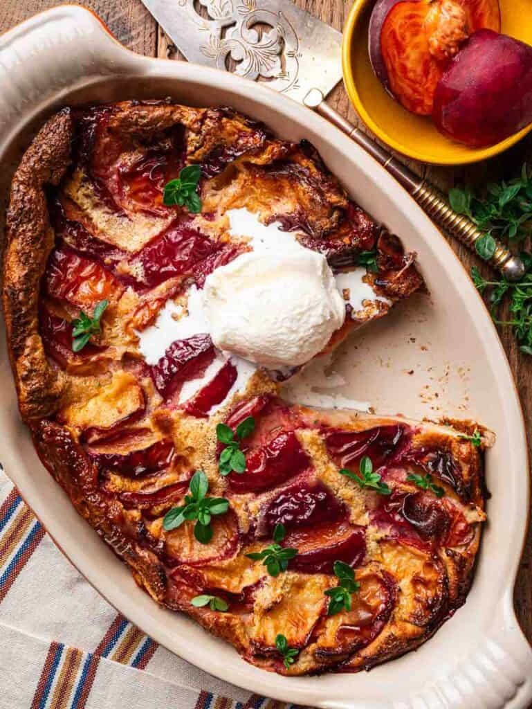 Peach clafoutis with a scoop of vanilla ice cream on top and a slice missing.