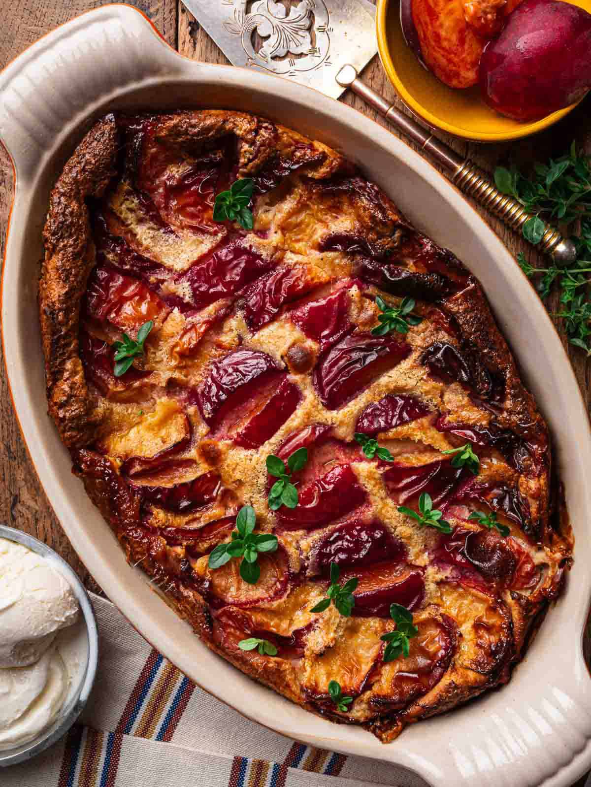 Golden baked peach clafoutis topped with fresh thyme with a scoop of ice cream on the side.