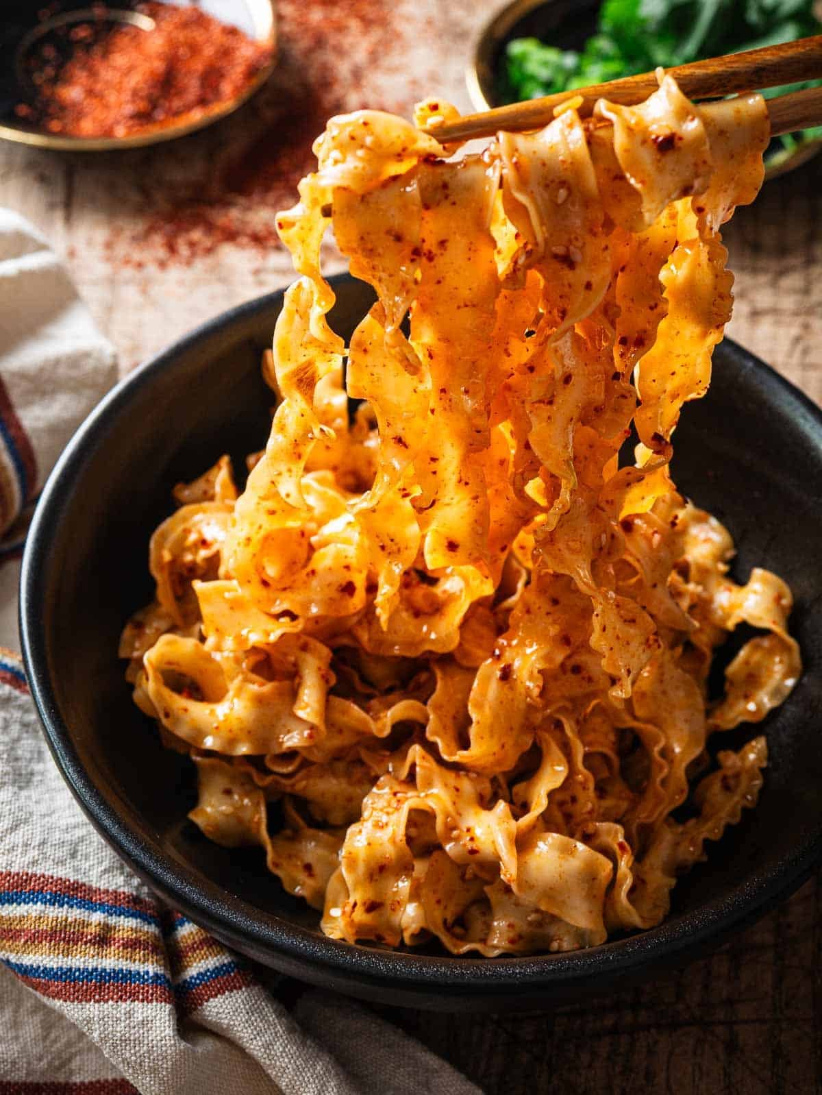 Spicy garlic noodles held with chopsticks over a black bowl.