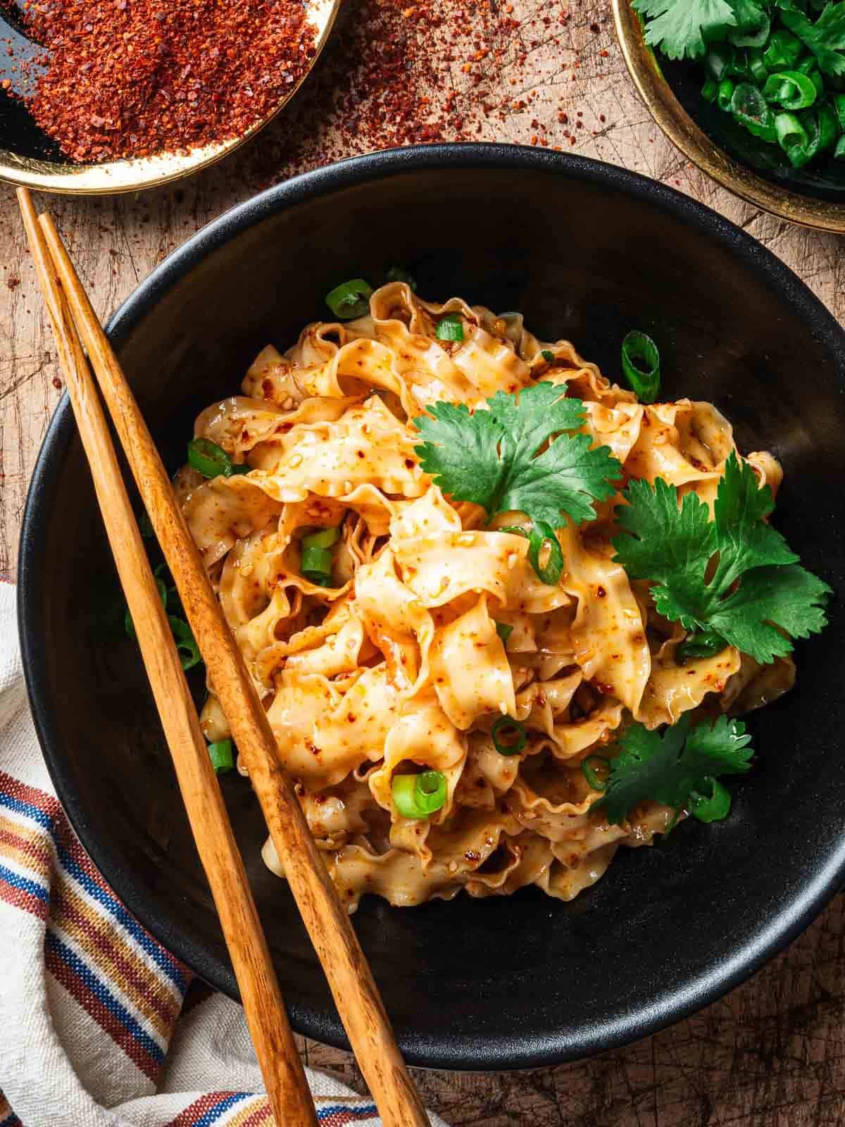 Garlic chili oil noodles in a black bowl with chopsticks on the side.