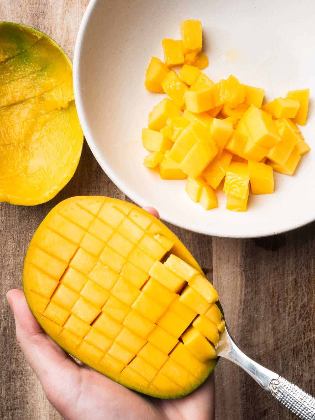 Hand with a spoon scooping cubes out of a mango.