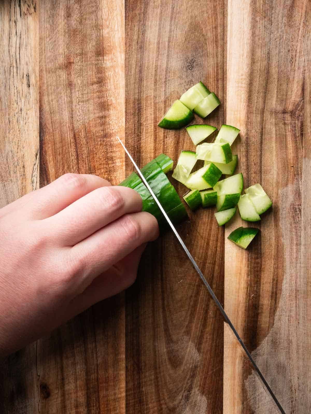 Hand with a kitchen knife dicing cucumber.