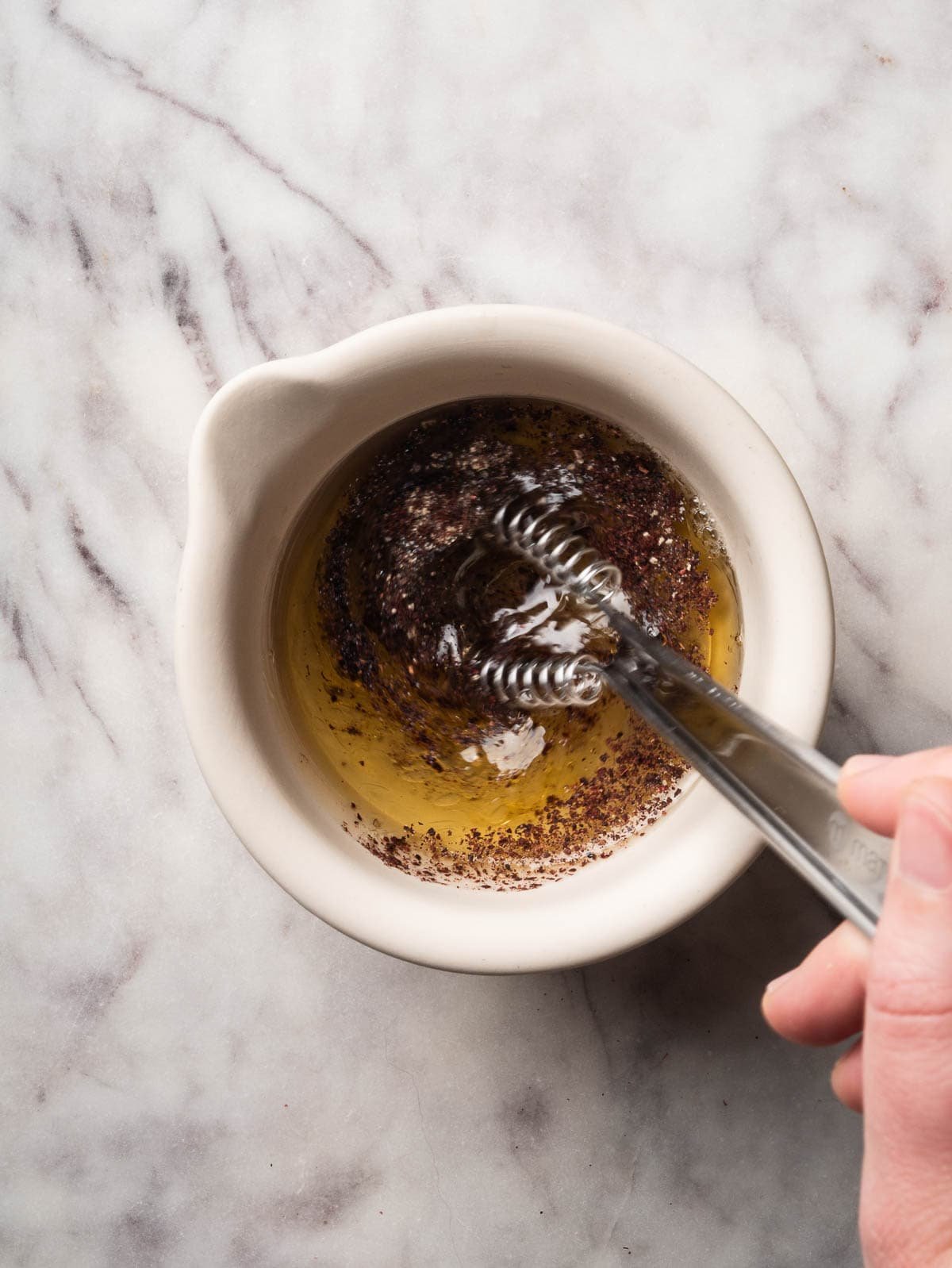 Hand with a whisk emulsifying sumac lime dressing.
