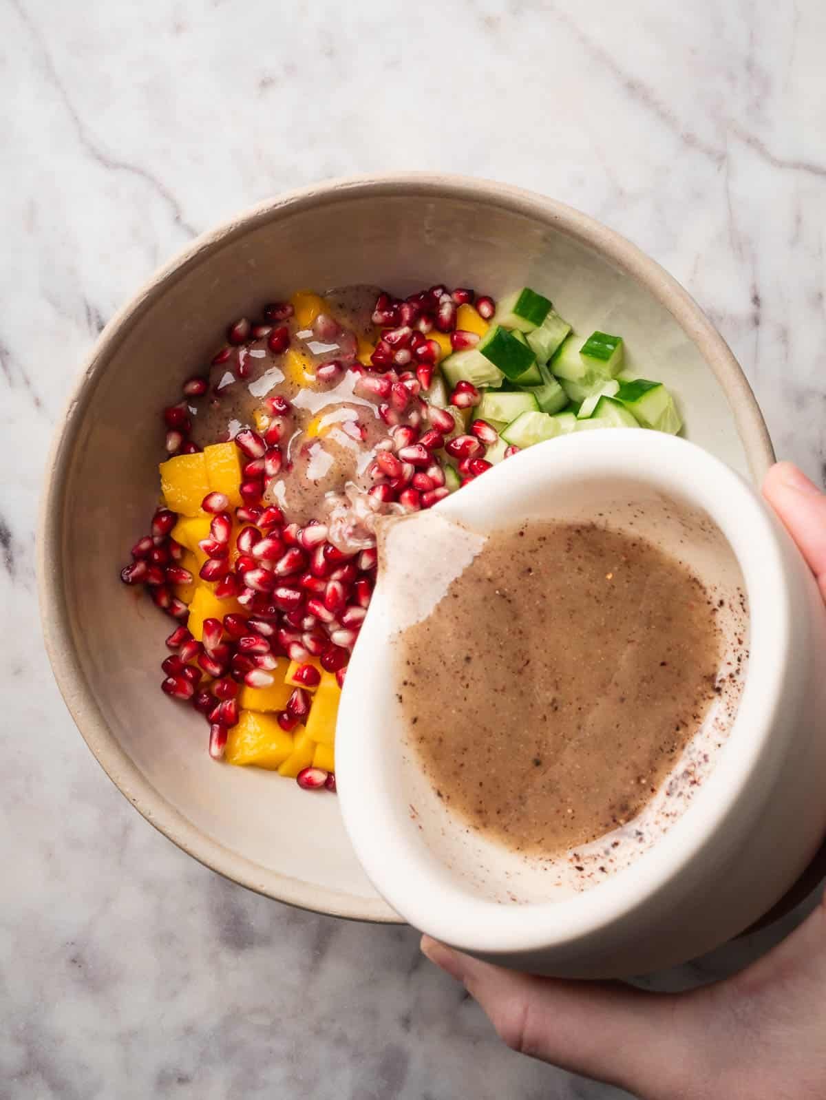 Lime-sumac dressing being poured on top of cucumber mango salad.