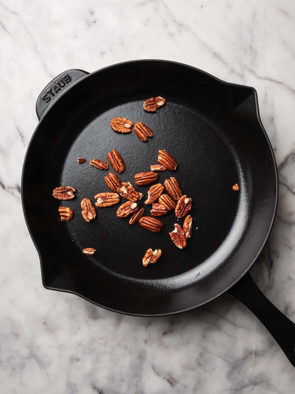 Pecans being toasted in a black skillet.