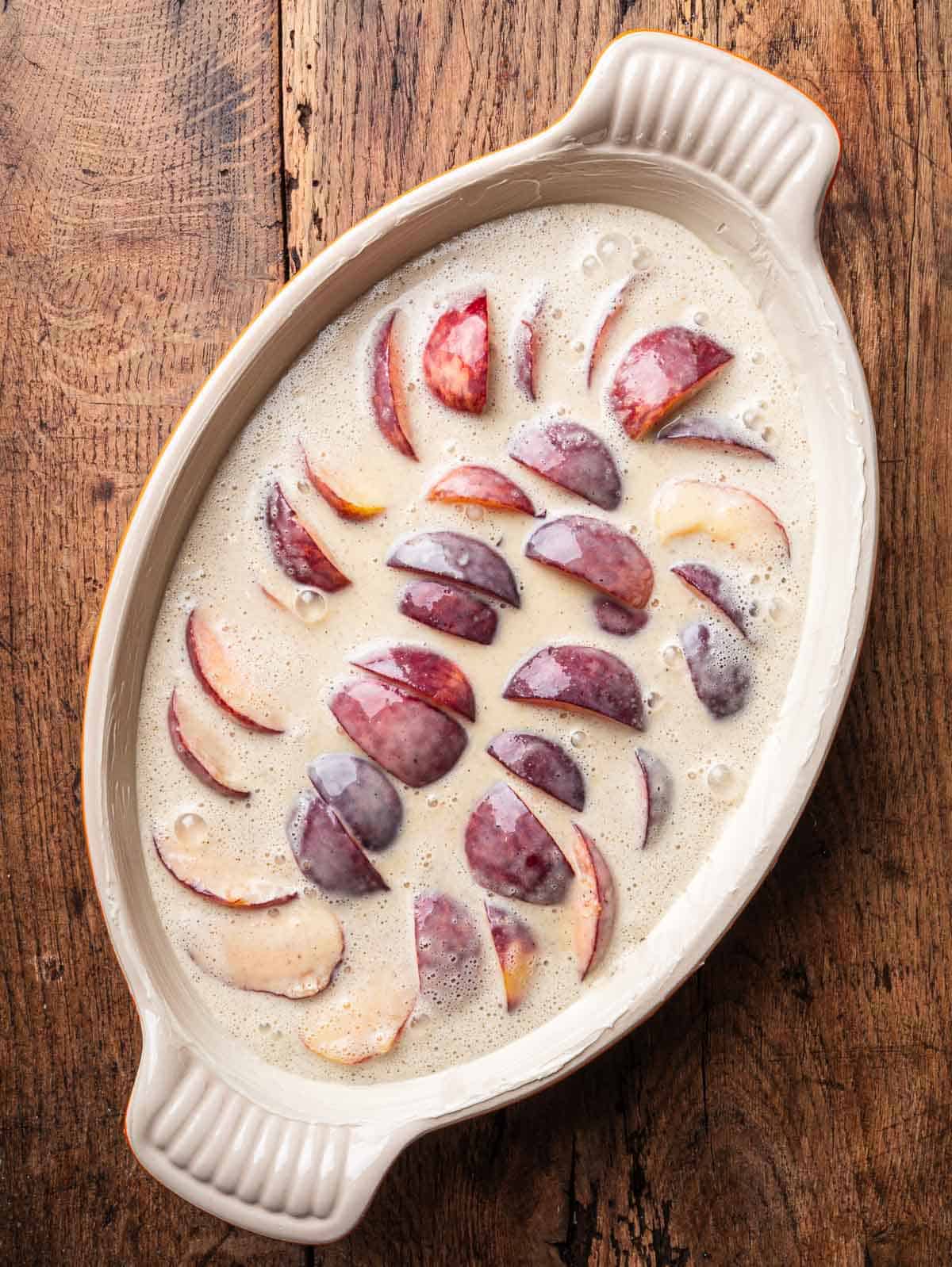 Unbaked peach clafoutis in an oval baking dish.
