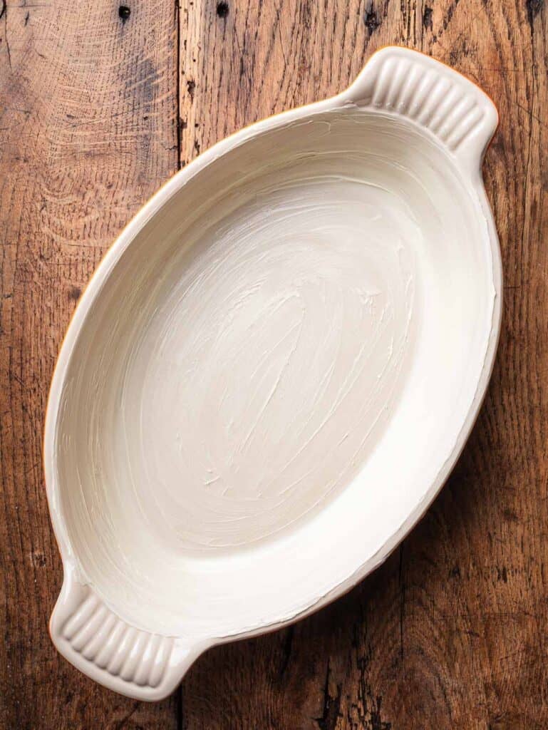 An oval baking dish greased with butter.