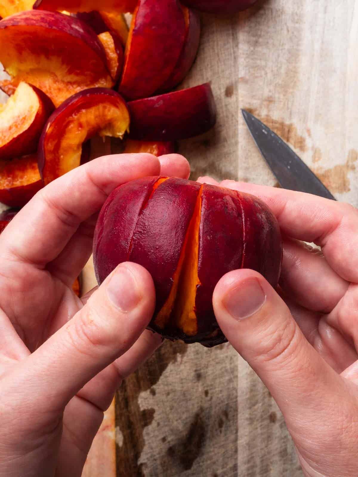 Hands holding a peach slices around the pit.