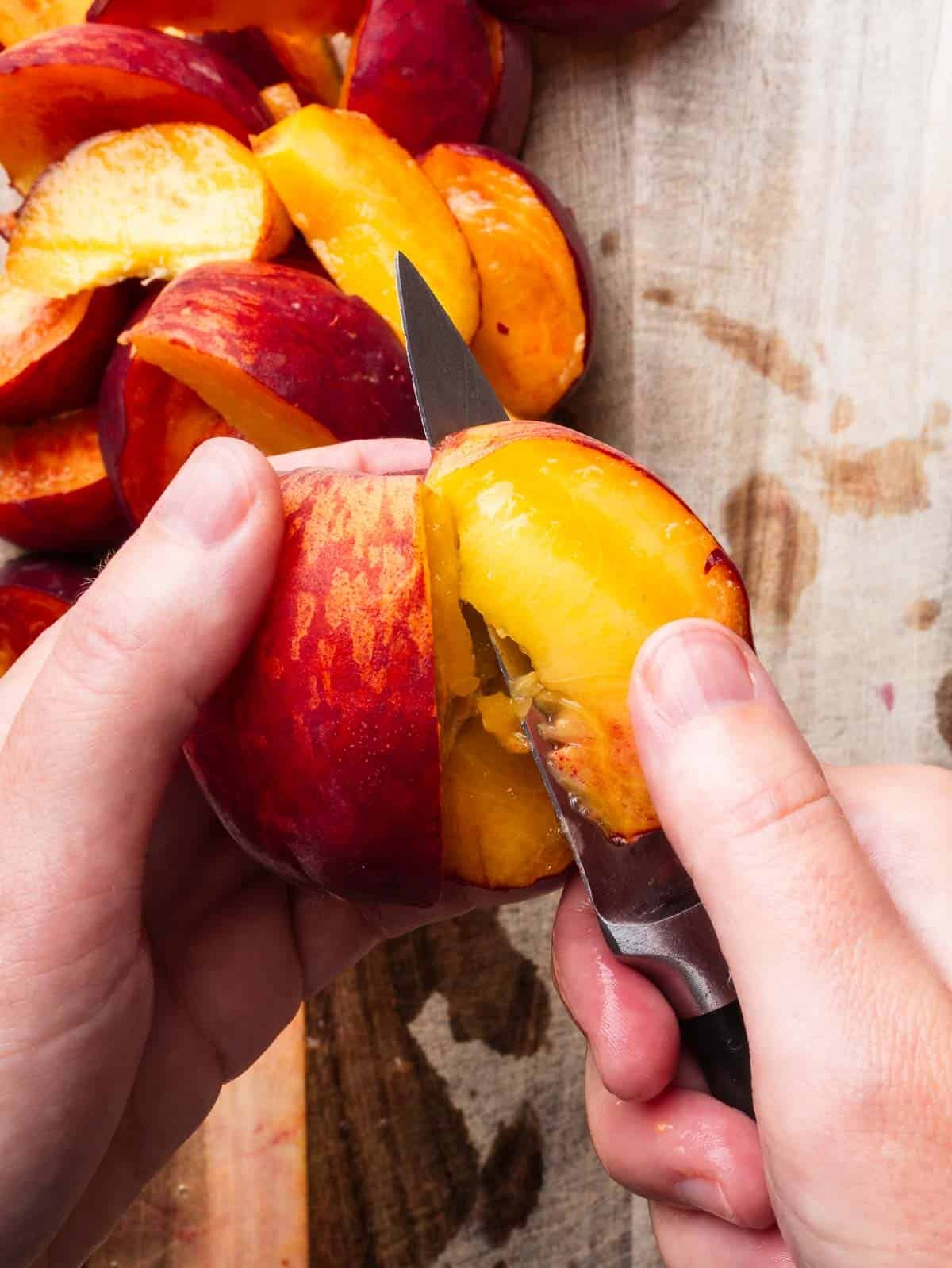 Hands with a pairing knife removing a slice from a peach.