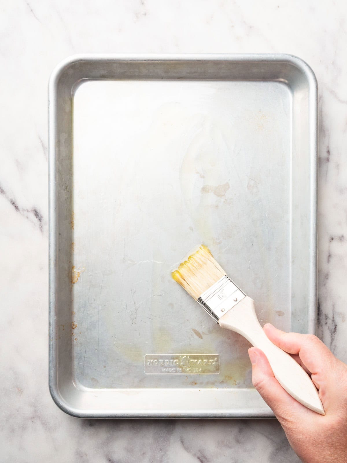 Hand brushing a baking sheet with olive oil.