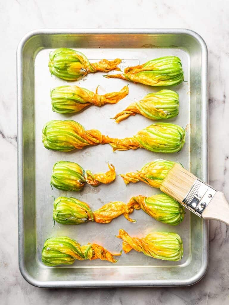 Stuffed zucchini blossom on a sheet pan brushed with olive oil.