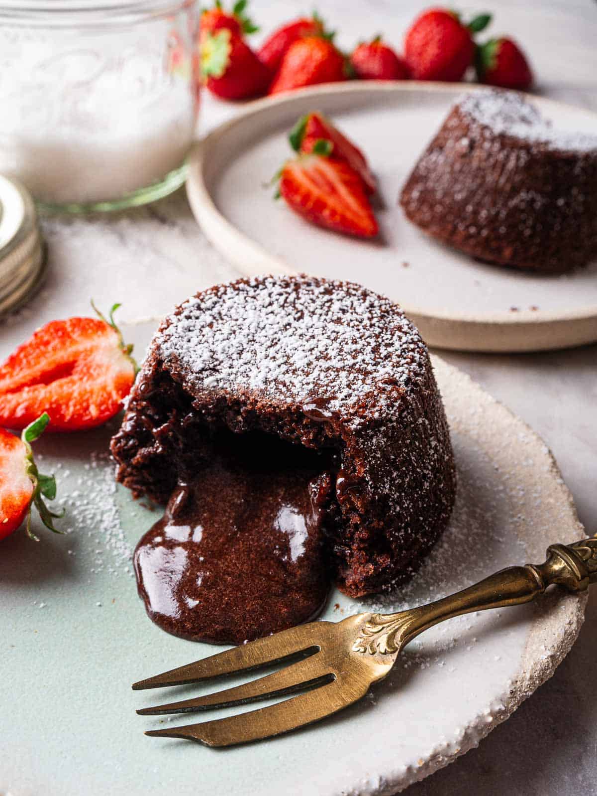 Chocolate lava cake on a small plate  with molten heart with strawberries on the side.