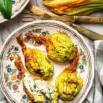 Roasted stuffed zucchini blossom in a vintage floral plate with one blossom cut in half.