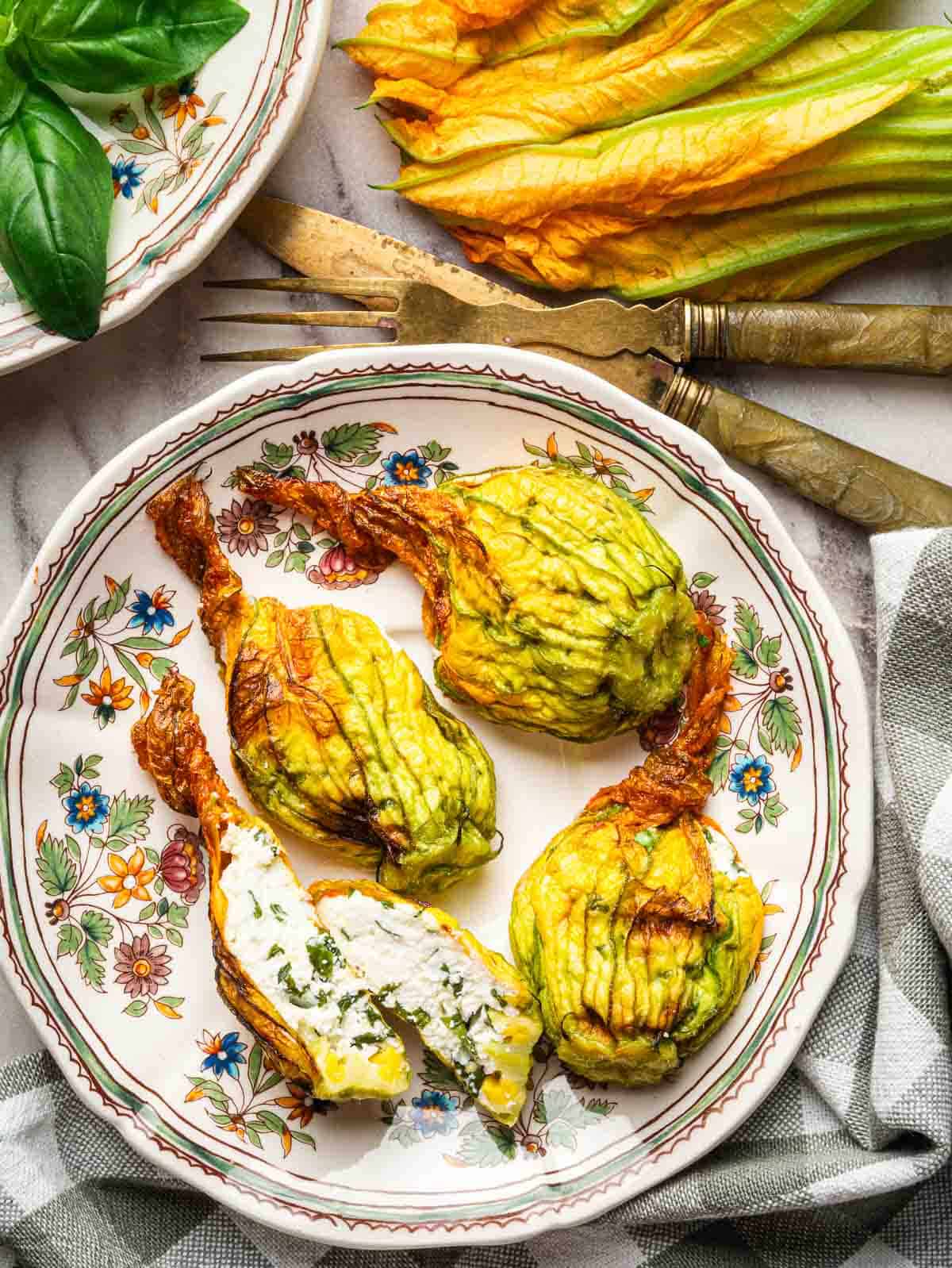 Roasted stuffed zucchini blossom in a vintage floral plate with one blossom cut in half.