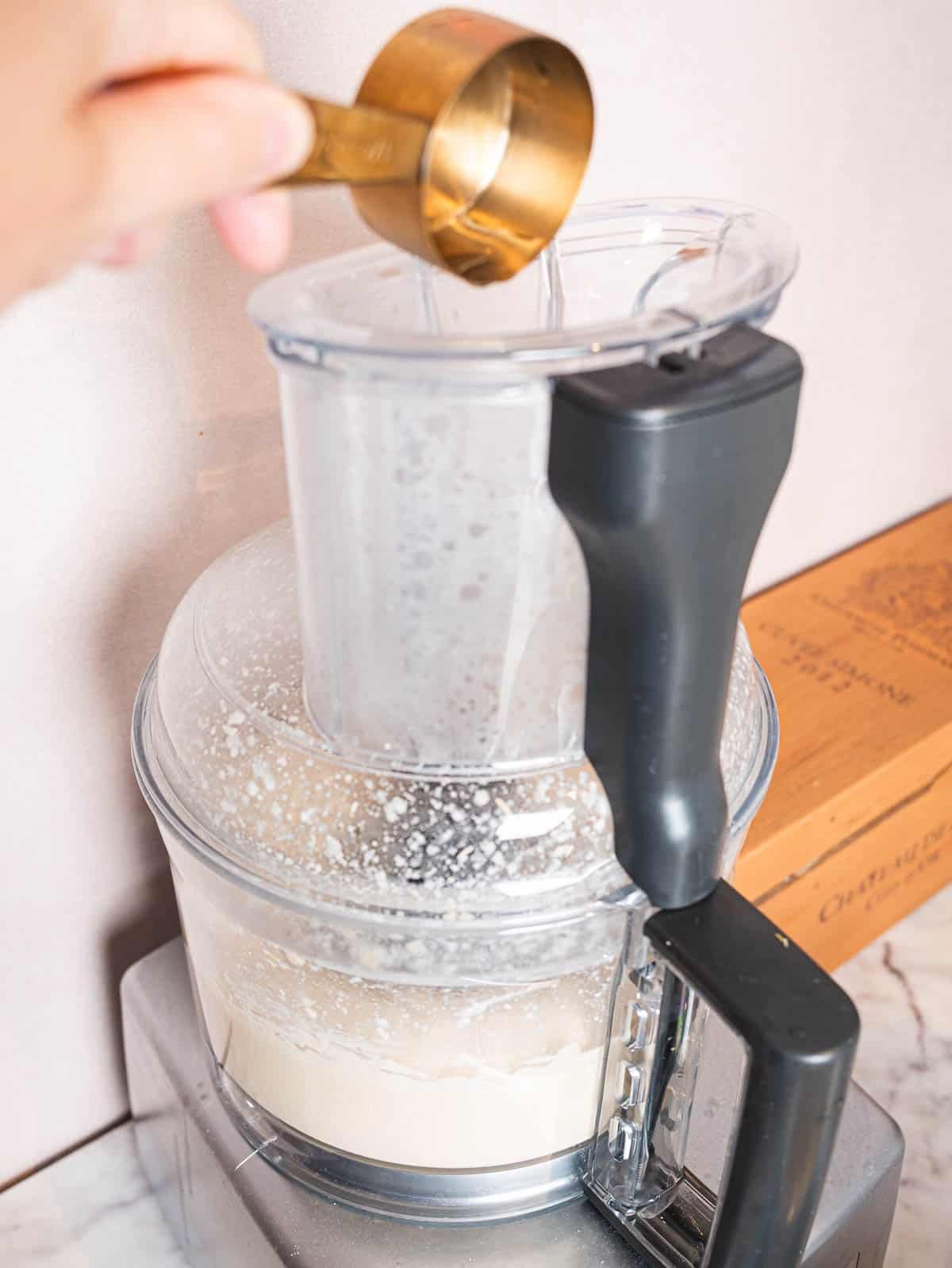 Iced water being added to hummus in a food processor.