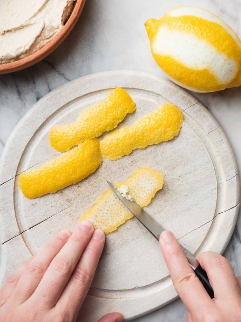 Hands scraping down the white part of a lemon peel with a pairing knife.