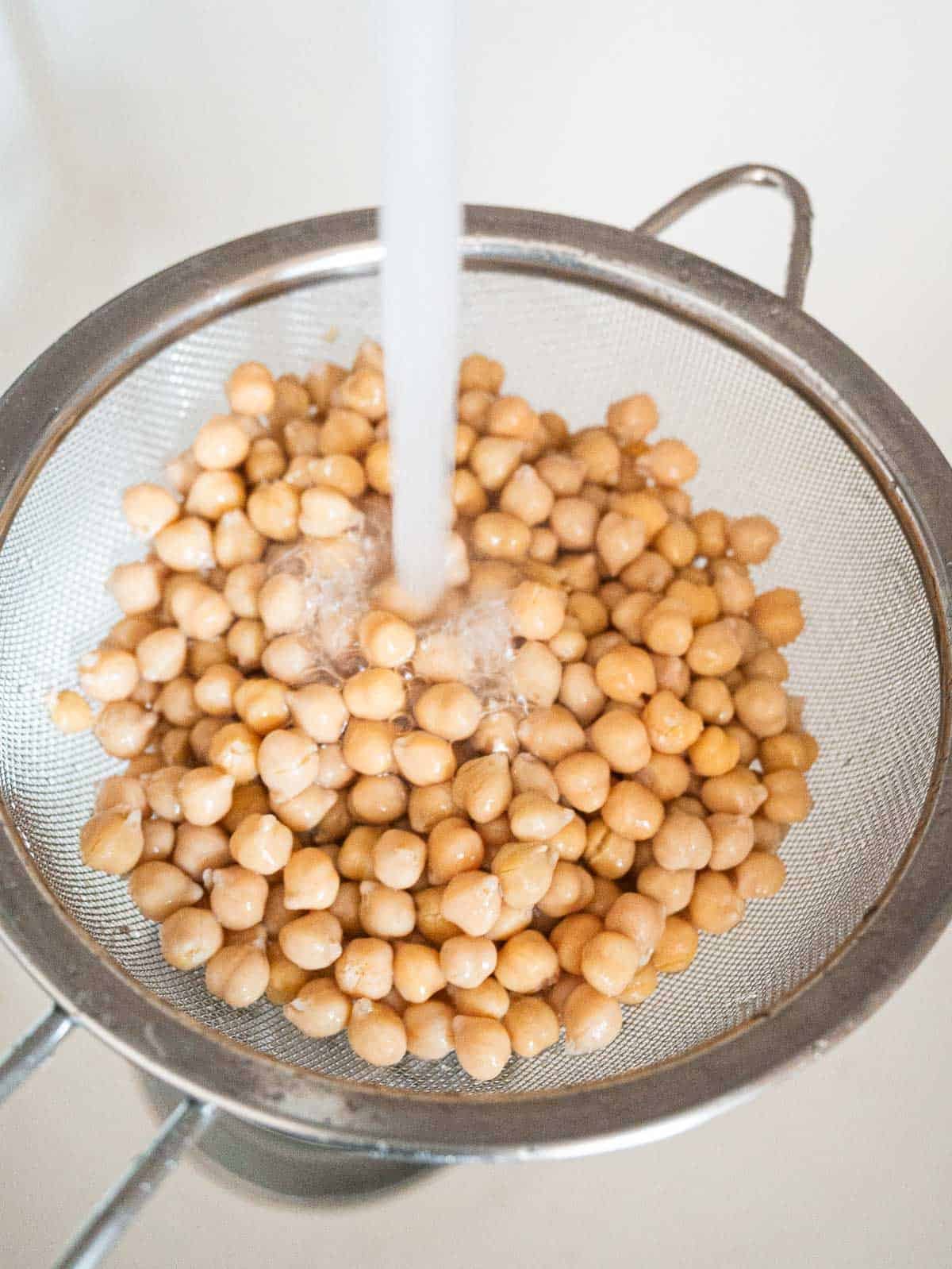 Chickpeas in a fine mesh strainer being rinsed under running water.
