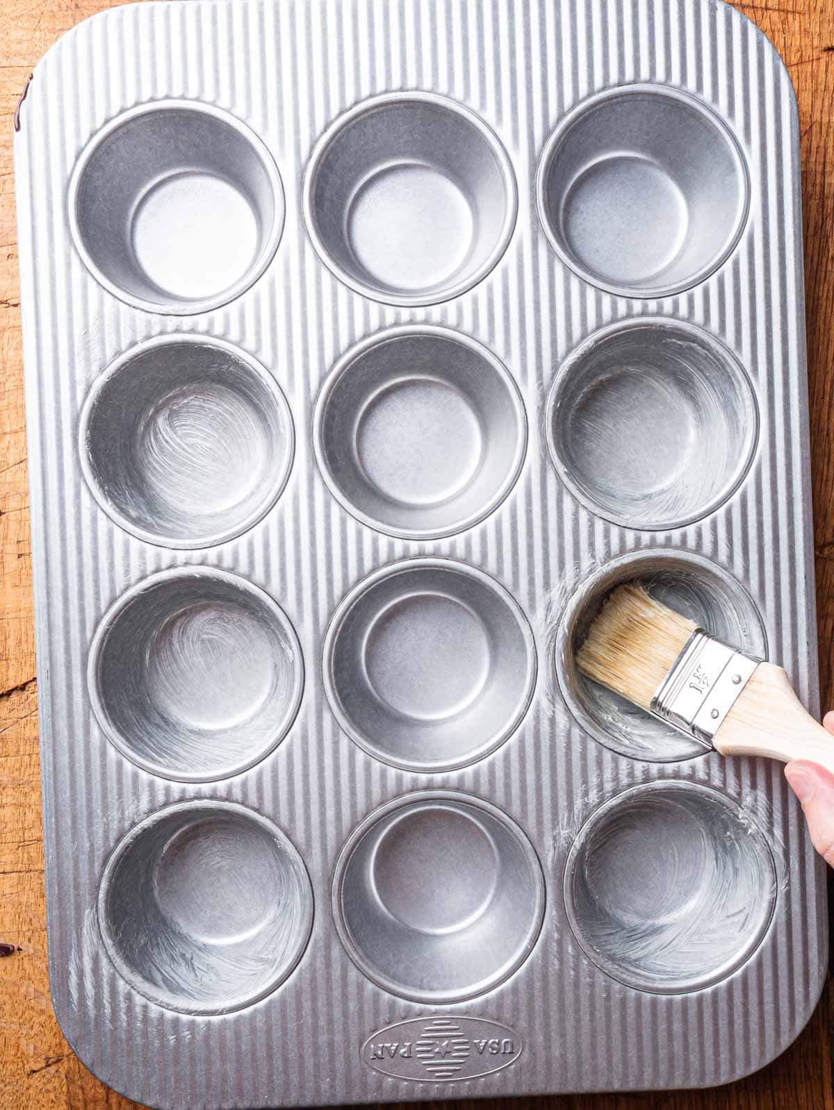 Hand brushing muffin tin with room-temperature butter.