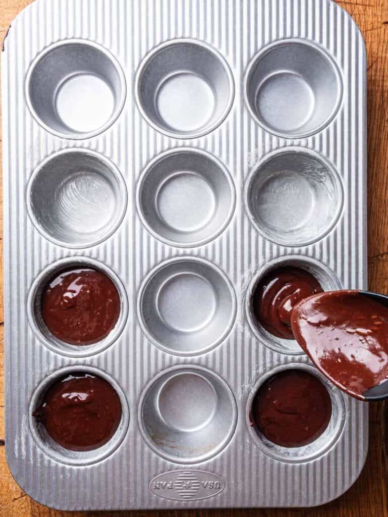Chocolate lava cake batter being poured into muffin tin.