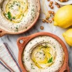 Lemon hummus topped with lemon strips on terra cotta bowls.