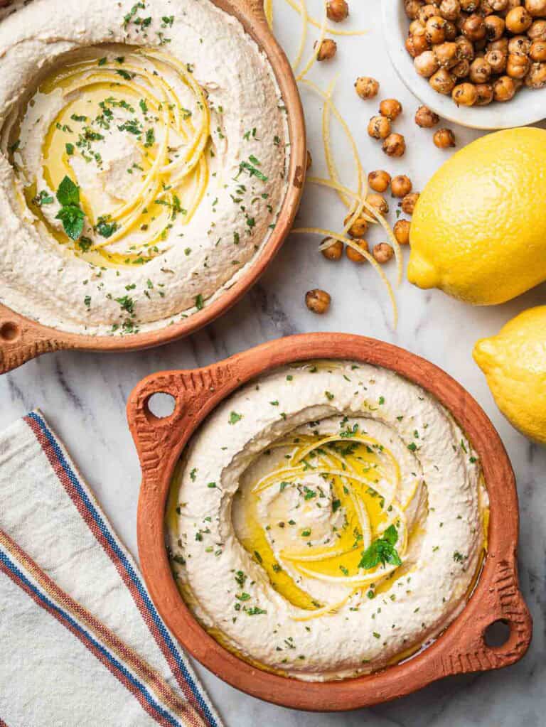 Lemon hummus topped with lemon strips on terra cotta bowls.
